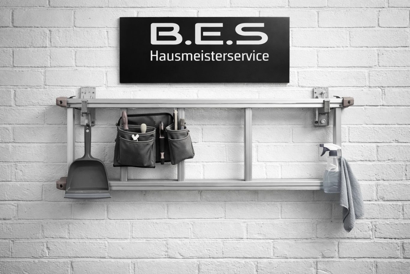 Hausmeisterdienste Schwarzes Schild mit „B.E.S. Hausmeisterservice“ über einer Leiter mit Werkzeugen.